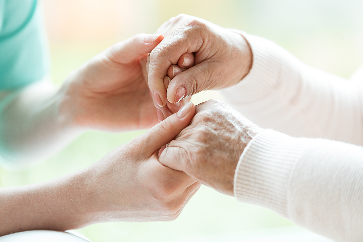 Hände einer Pflegefachperson, welche die Hände einer Seniorin hält