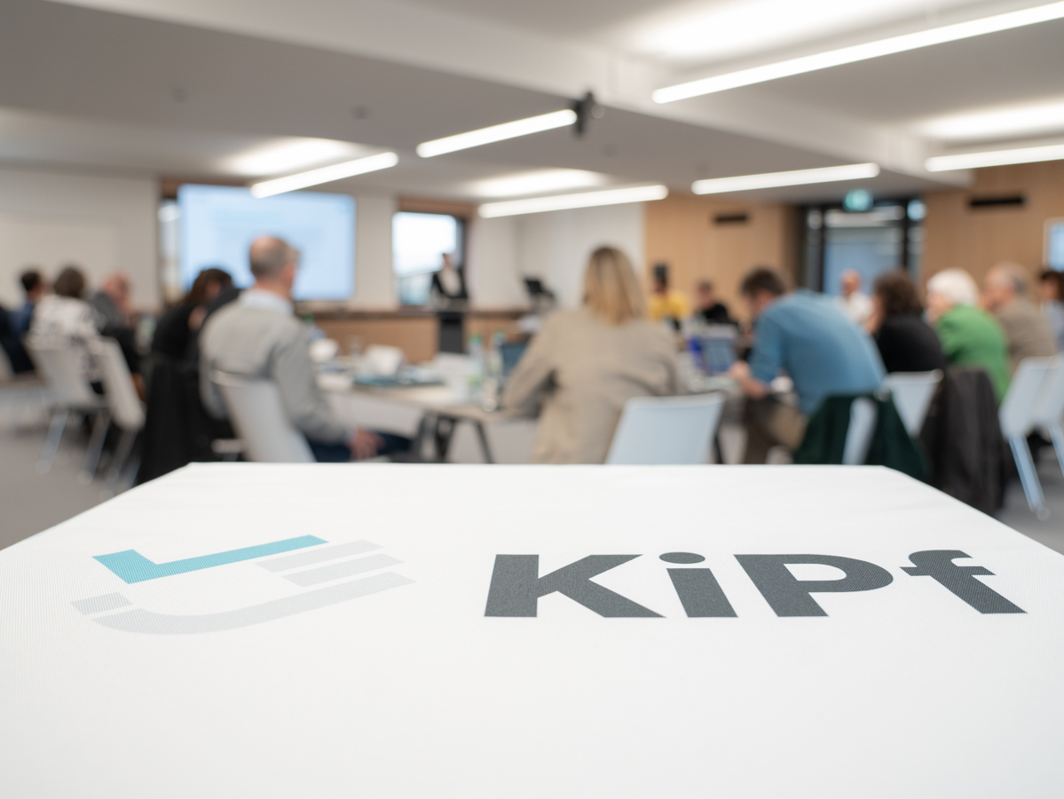 Würfel mit KiPf Logo im Vordergrund und im Hintergrund sieht man die Rücken von Personen unscharf
