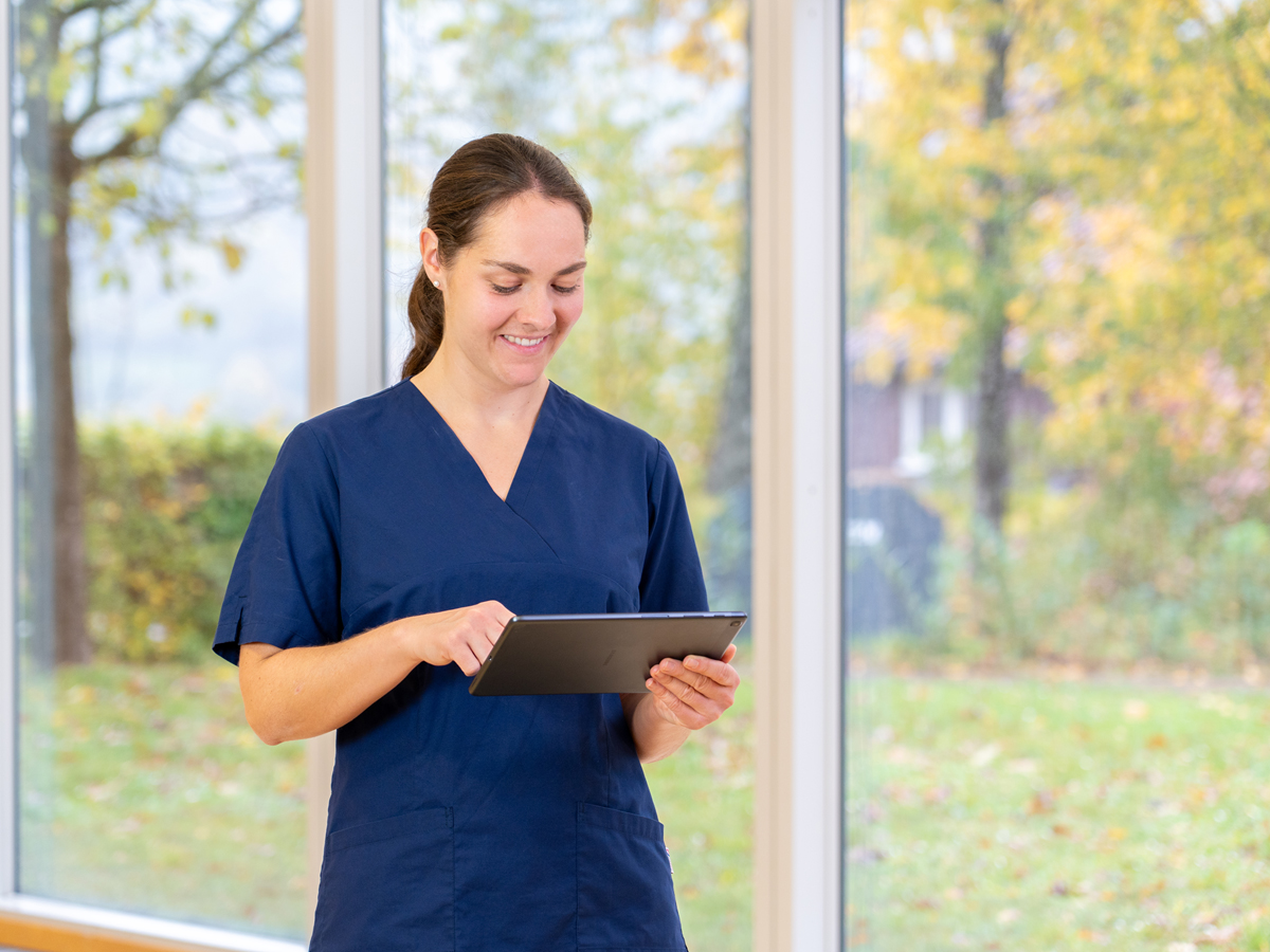Eine Pflegefachperson hält ein Tablet in der Hand und tippt mit einer Hand auf das Tablet.