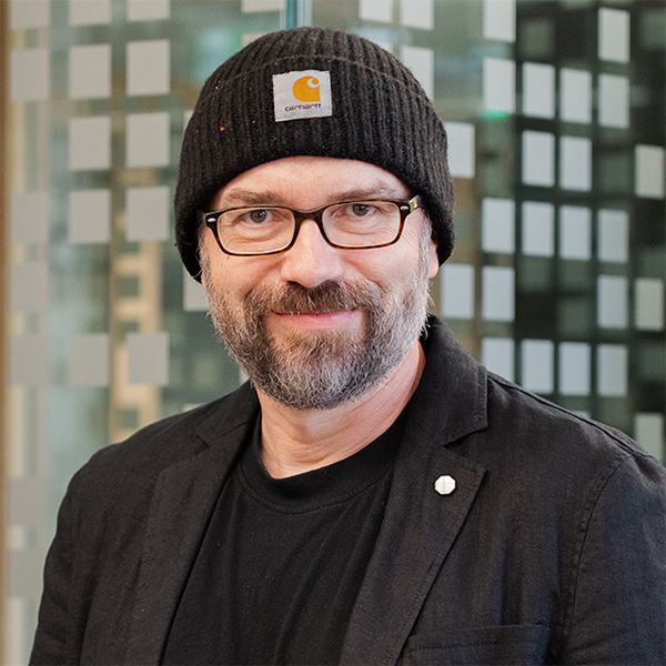Porträtfoto von Christian Wieber. Älterer Mann mit Vollbart. Trägt eine Brille, Mütze und hat dunkelbraune Augen.