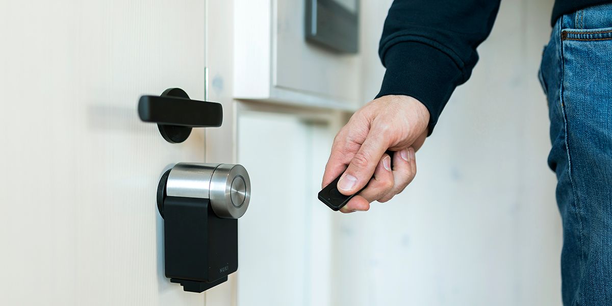 Eine Hand hält eine Fernbedienung für eine elektrische Türöffnung in der Hand an eine Tür mit ausgetauschtem Metallzylinder