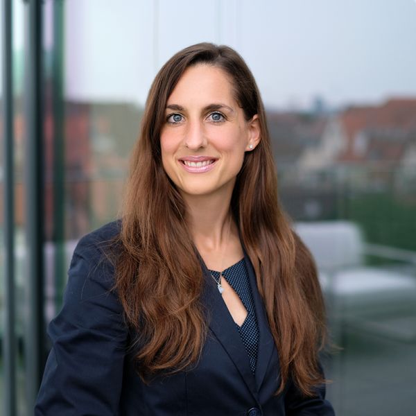 Porträtfoto von Dr. Ana Babac. Lange braune Haare, graue Augen und trägt dunkelblaues Kostüm.
