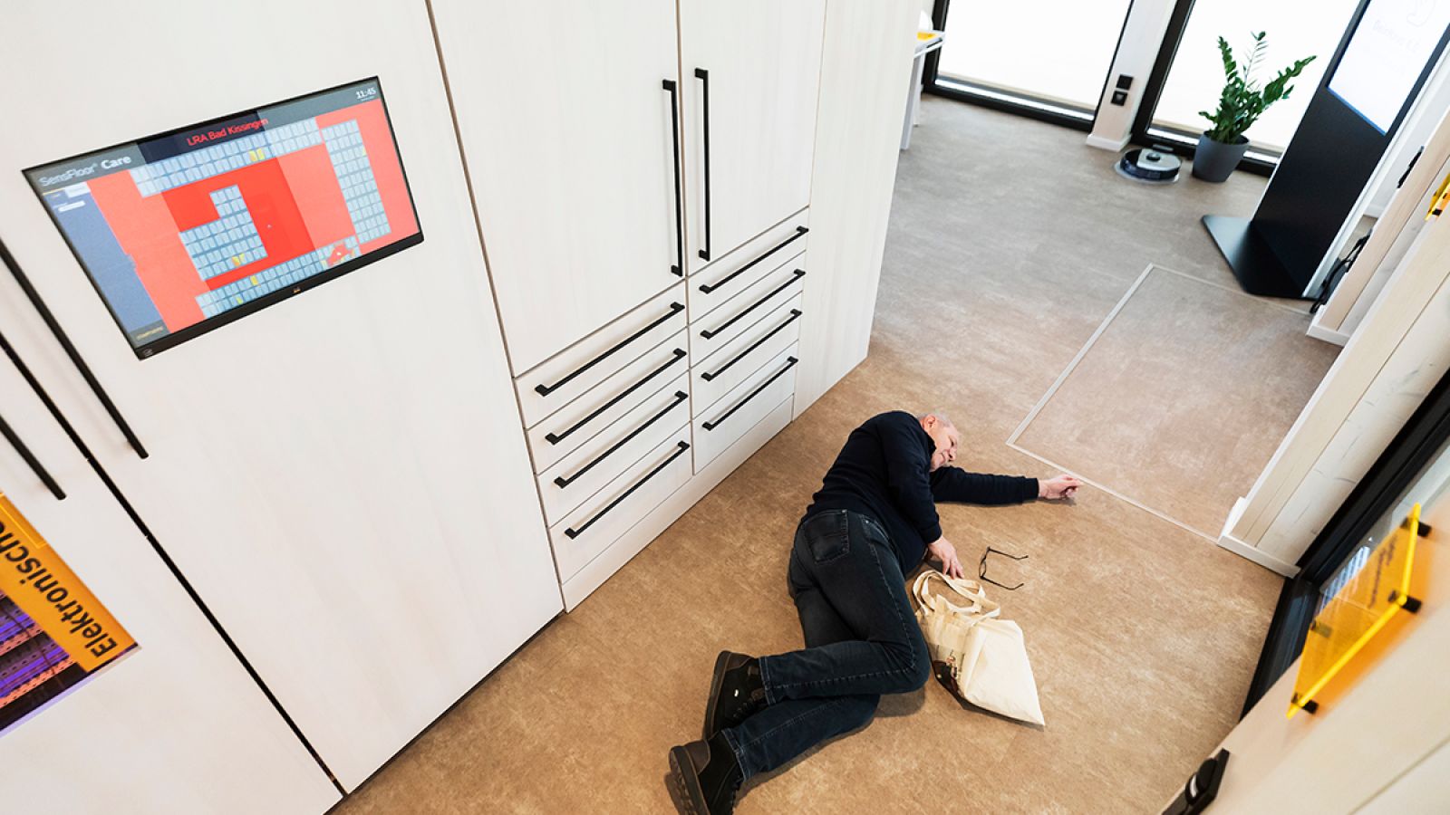 Ein Mann liegt regungslos auf dem Boden. Über ihn ist in einem Schrank ein Bildschirm, der rot leuchtet.