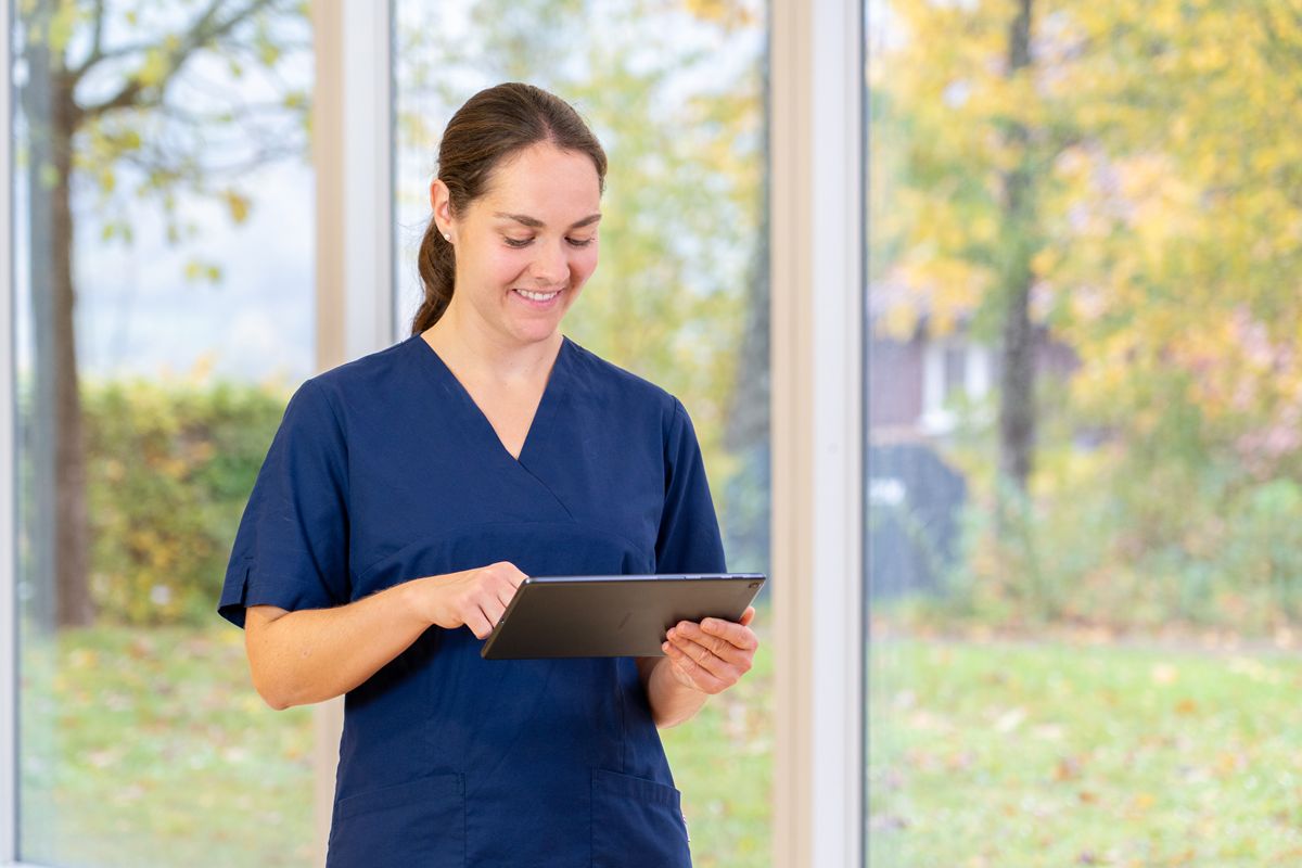 Eine Pflegefachperson hält ein Tablet in der Hand und tippt mit einer Hand auf das Tablet.