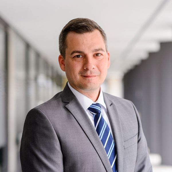 Porträtfoto von Sebastian Hilke. Mann mit dunkelbbraunen Haaren und dunkelbraunen Augen im Anzug.