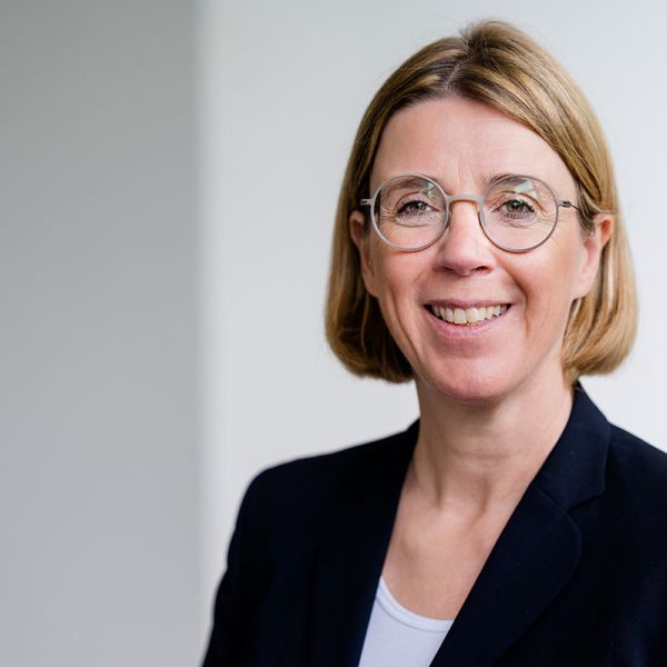 Porträtfoto von Ute Wolf. Ältere Frau mit blondem Bob, Brille und hellbraunen Augen im Blazer..