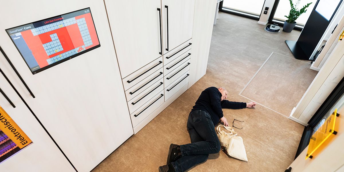 Ein Mann liegt regungslos auf dem Boden. Über ihn ist in einem Schrank ein Bildschirm, der rot leuchtet.