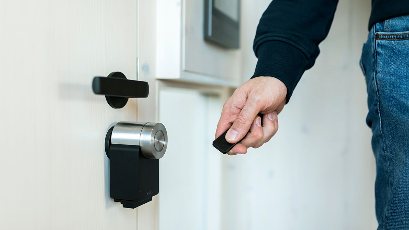 Eine Hand hält eine Fernbedienung für eine elektrische Türöffnung in der Hand an eine Tür mit ausgetauschtem Metallzylinder